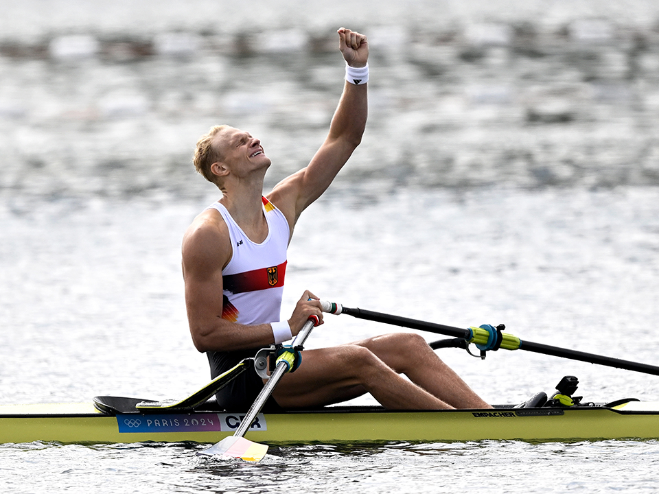 Ruderer Oliver Zeidler sitzt in seinem Boot und streckt jubelnd den linken Arm in die Luft.