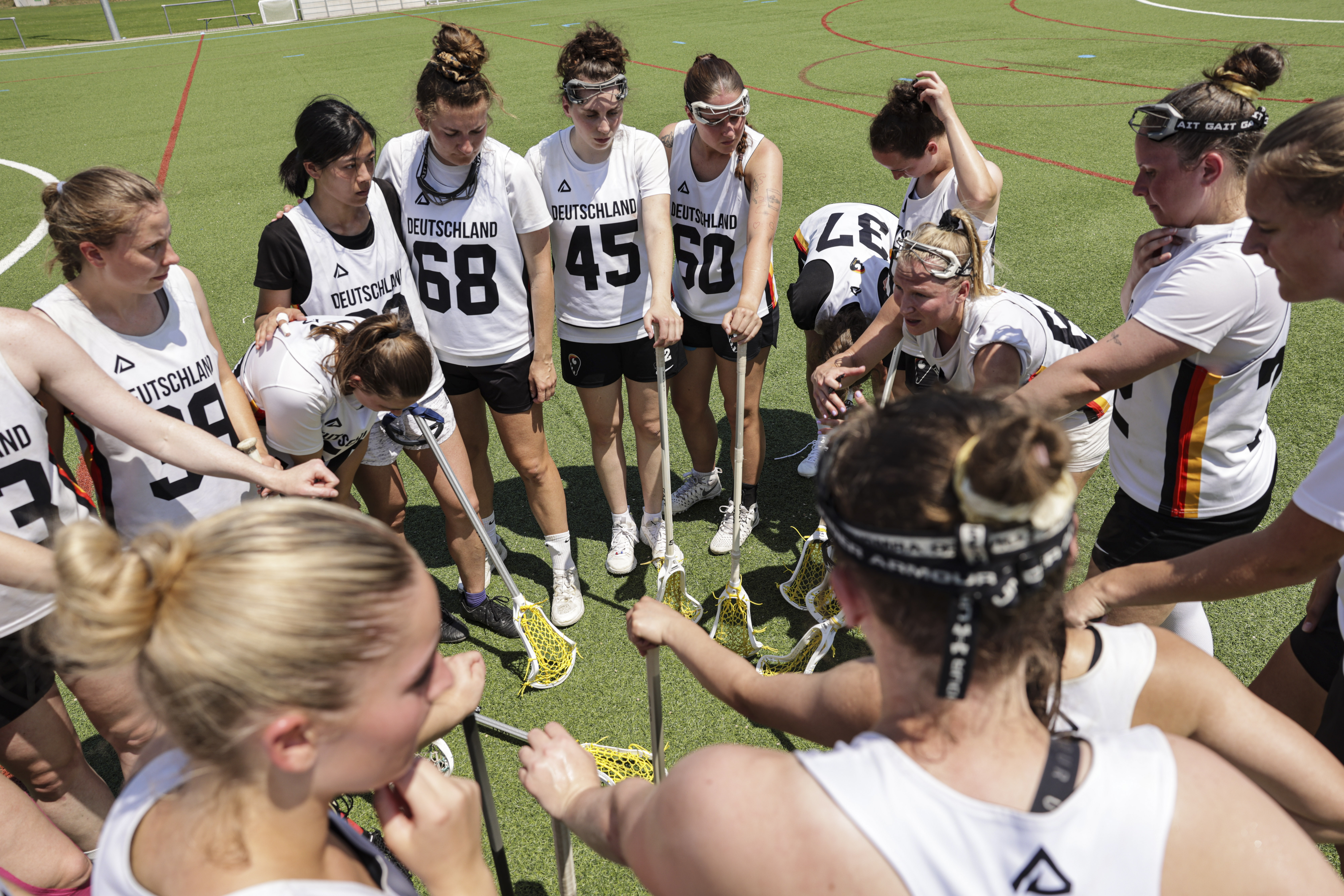 Lacrosse-Spielerinnen der Nationalmannschaft stehen in einem Kreis zusammen und halten ihre Lacrosse-Schläger in die Mitte.